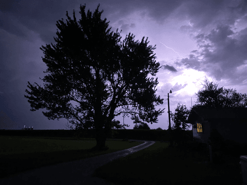 Thunderstorm and lightning behind a farmhouse and tree.